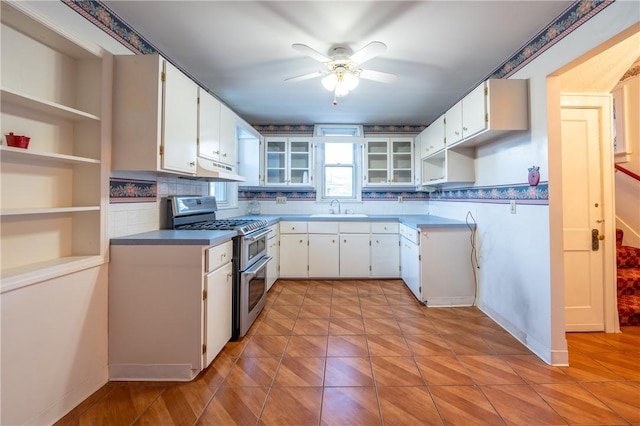 kitchen with a ceiling fan, white cabinetry, under cabinet range hood, range with two ovens, and a sink