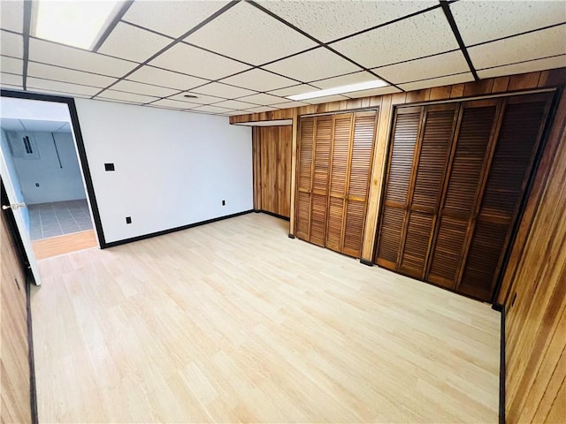 finished basement with wooden walls, baseboards, a drop ceiling, and light wood finished floors