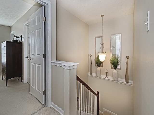 hallway with light colored carpet, a textured ceiling, and an upstairs landing