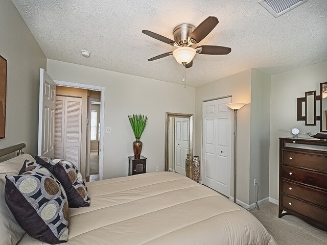carpeted bedroom with a ceiling fan, a textured ceiling, visible vents, and baseboards