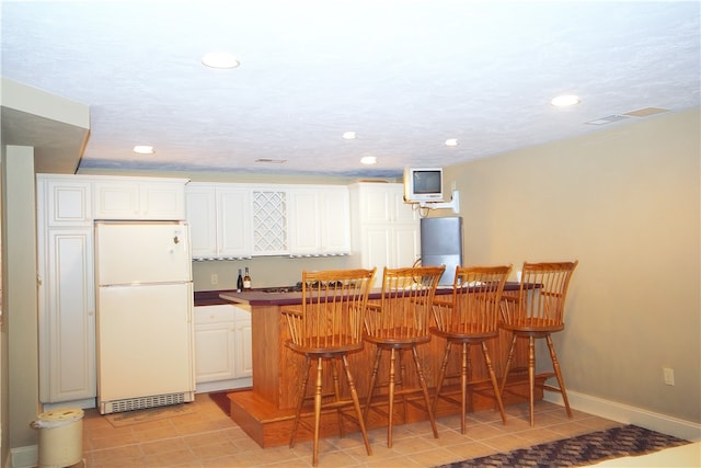 interior space with white cabinets, a kitchen breakfast bar, freestanding refrigerator, recessed lighting, and light tile patterned floors