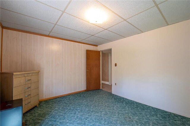 spare room featuring baseboards, carpet, wooden walls, and a paneled ceiling