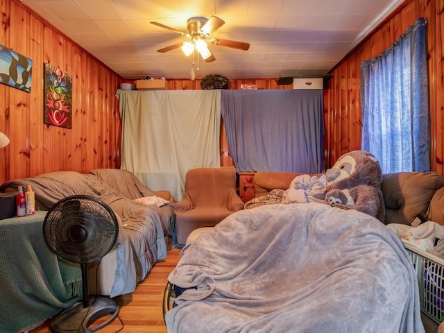 bedroom with ceiling fan, wood walls, and light wood-style flooring
