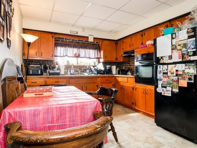 kitchen with brown cabinetry, a paneled ceiling, tasteful backsplash, under cabinet range hood, and black appliances