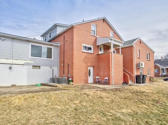 back of property featuring a yard, brick siding, a wall unit AC, and central AC unit