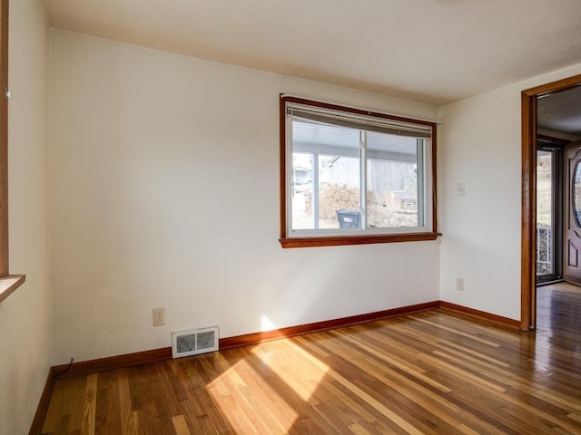 empty room featuring visible vents, baseboards, wood finished floors, and a wealth of natural light
