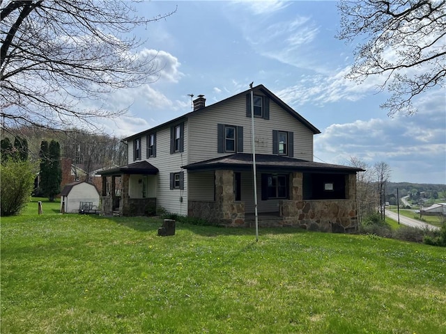back of house featuring a lawn, a chimney, stone siding, and a storage shed