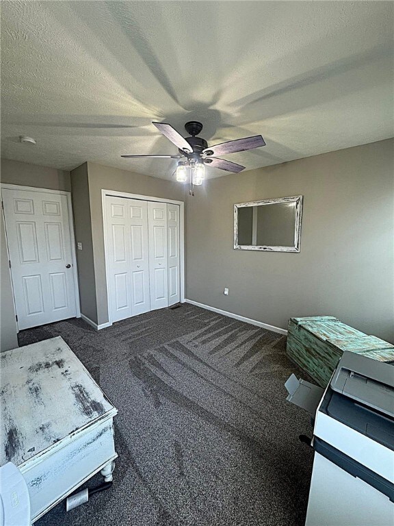 bedroom with a textured ceiling, dark carpet, a ceiling fan, baseboards, and a closet