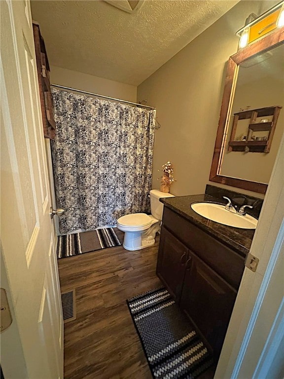bathroom with vanity, toilet, a textured ceiling, wood finished floors, and visible vents