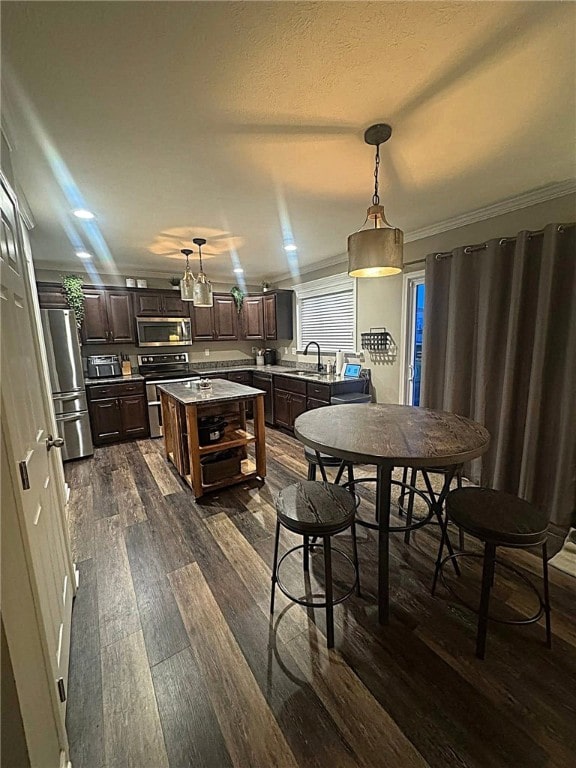 kitchen featuring dark brown cabinetry, a sink, stainless steel appliances, decorative light fixtures, and dark wood-style floors