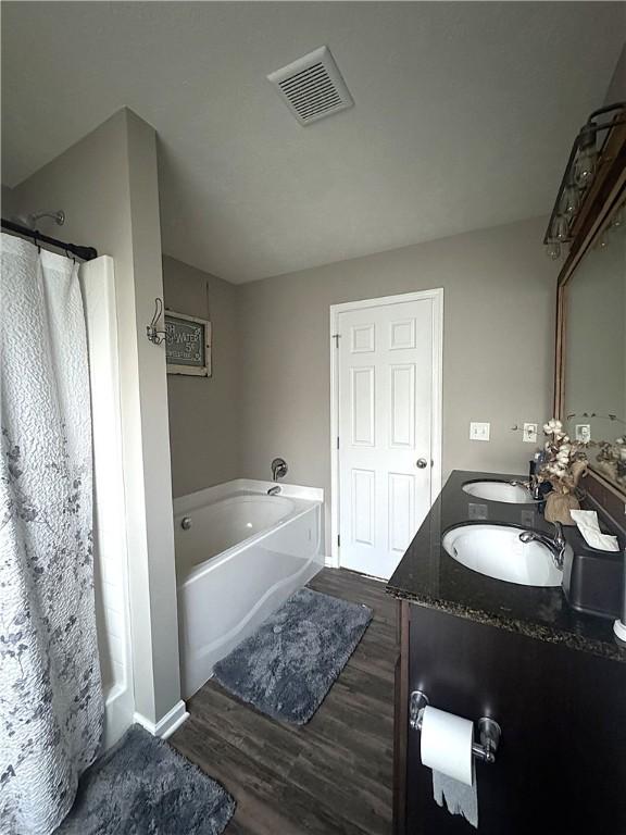 full bath with visible vents, a garden tub, double vanity, wood finished floors, and a sink