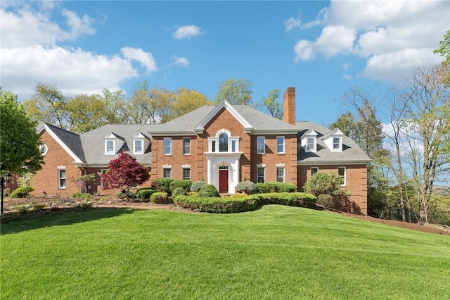 georgian-style home with brick siding, a front lawn, and a chimney