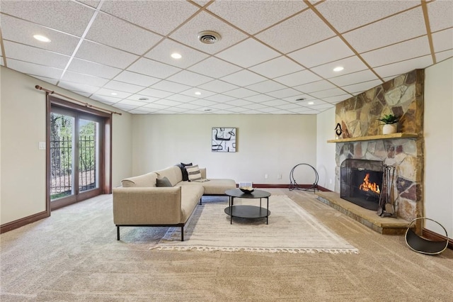 carpeted living room with baseboards, a drop ceiling, a stone fireplace, and visible vents
