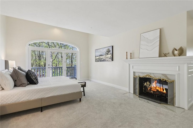 bedroom featuring access to exterior, baseboards, light colored carpet, french doors, and a fireplace with flush hearth
