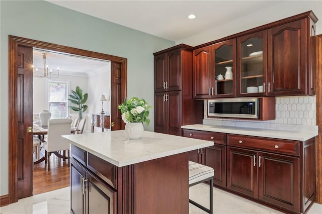 kitchen featuring decorative backsplash, glass insert cabinets, light countertops, stainless steel microwave, and a notable chandelier
