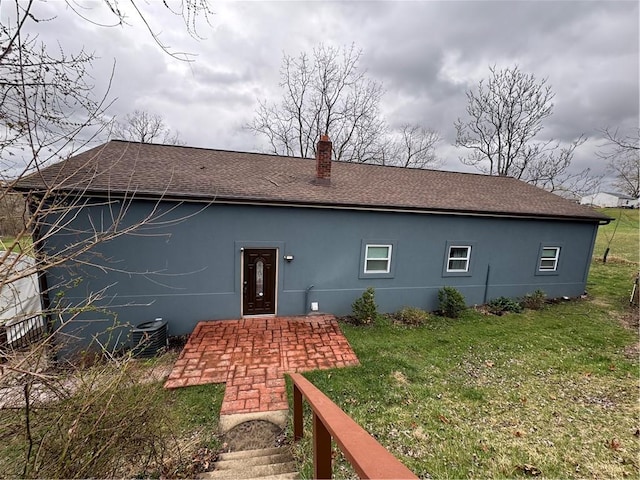 rear view of house with central AC unit, roof with shingles, a yard, and a chimney