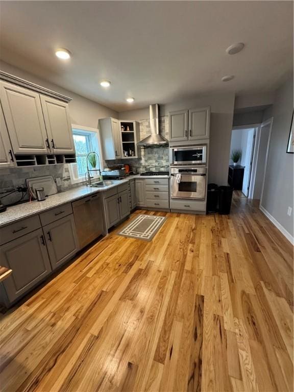 kitchen with gray cabinets, tasteful backsplash, a sink, stainless steel appliances, and wall chimney exhaust hood