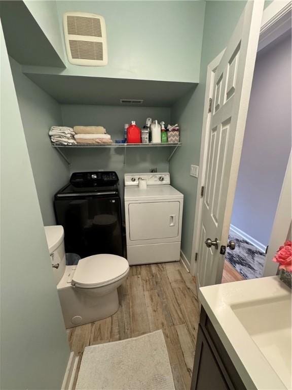 half bathroom with wood finished floors, washing machine and dryer, toilet, and vanity