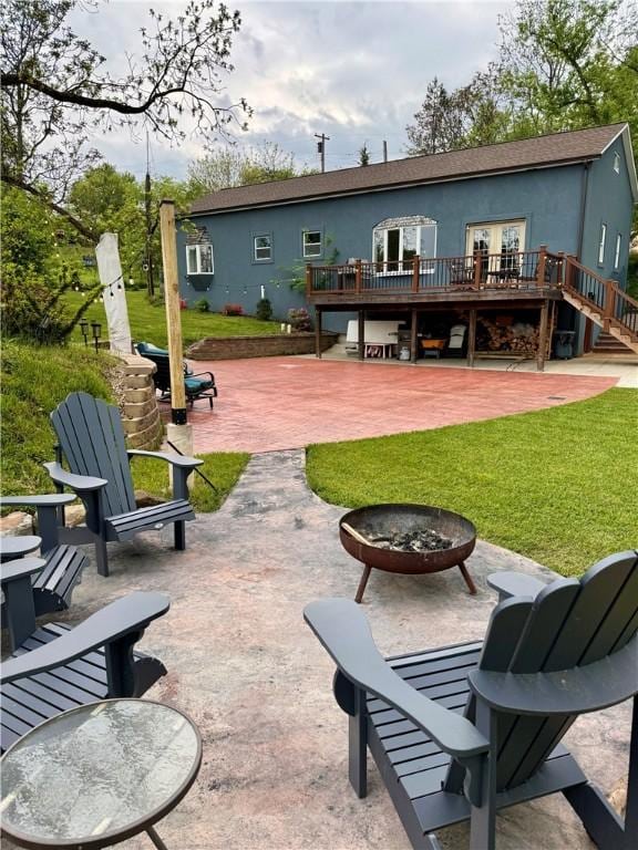 rear view of property with a fire pit, a deck, stucco siding, a patio area, and a yard