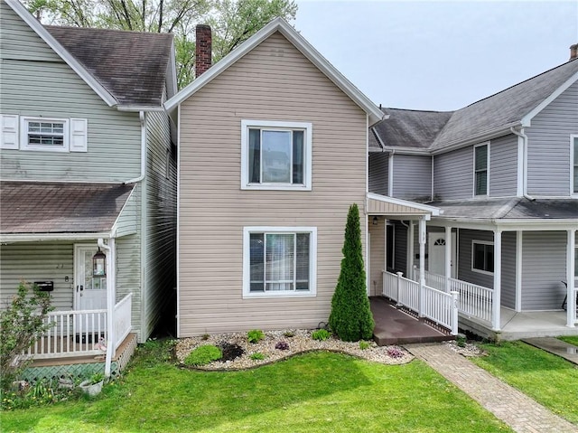 view of front facade with a porch, a front lawn, and a chimney