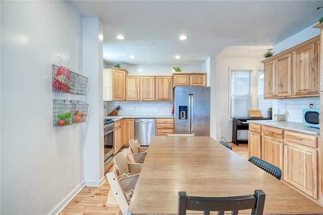 kitchen featuring appliances with stainless steel finishes, light brown cabinets, light countertops, decorative backsplash, and light wood-type flooring