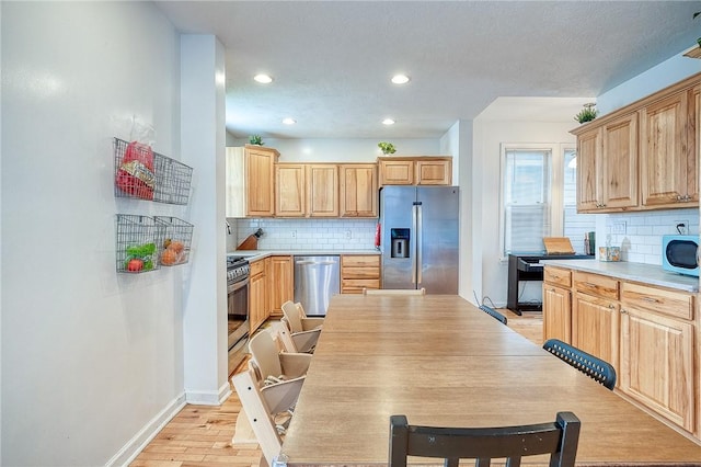 kitchen featuring baseboards, appliances with stainless steel finishes, backsplash, and light wood-type flooring