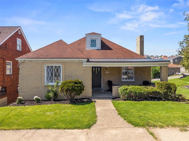 view of front of property featuring brick siding, a chimney, a front yard, and a porch