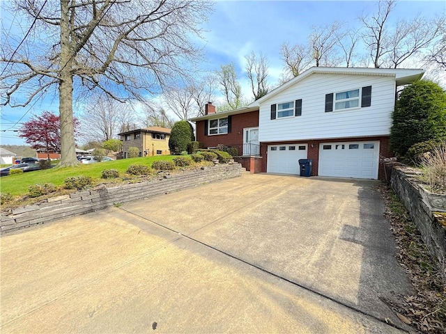 split level home with concrete driveway, brick siding, a chimney, and a garage