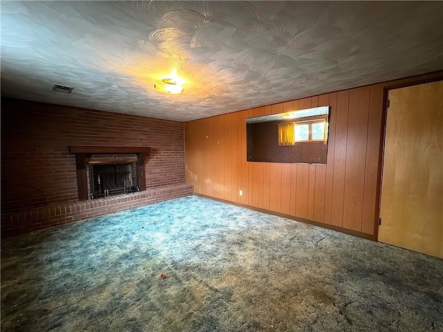 unfurnished living room with visible vents, wood walls, a brick fireplace, baseboards, and carpet flooring