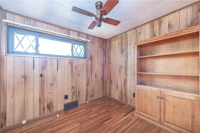 spare room with ceiling fan, visible vents, wood walls, and wood finished floors