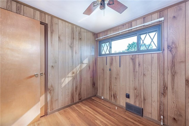 unfurnished room with visible vents, wood walls, light wood-style flooring, and ceiling fan