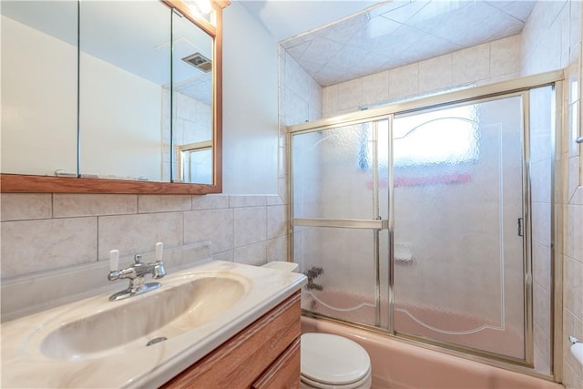 bathroom with shower / bath combination with glass door, vanity, toilet, and tile walls