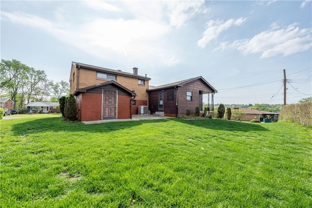 rear view of house featuring a lawn, central AC unit, and brick siding