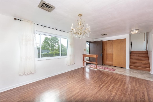 unfurnished living room with visible vents, stairs, wood finished floors, and a chandelier