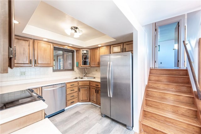 kitchen featuring appliances with stainless steel finishes, a sink, a raised ceiling, light wood finished floors, and decorative backsplash