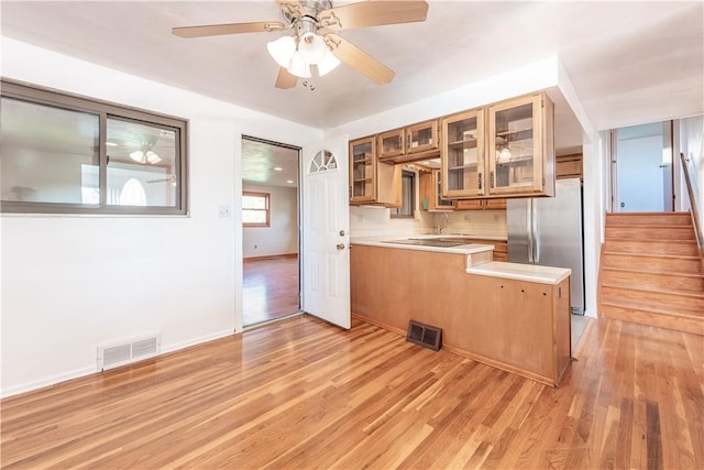 kitchen featuring brown cabinetry, visible vents, light countertops, freestanding refrigerator, and a peninsula