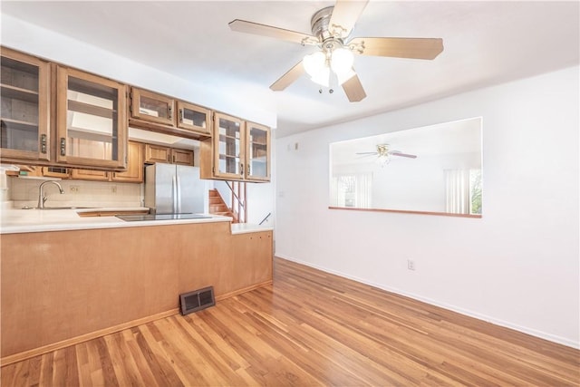 kitchen featuring brown cabinets, light countertops, light wood-style flooring, freestanding refrigerator, and a ceiling fan