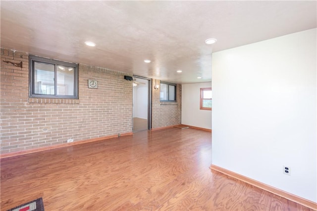 spare room featuring baseboards, recessed lighting, wood finished floors, and brick wall