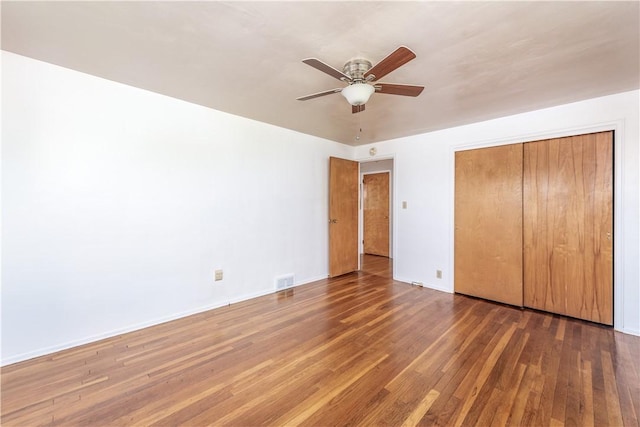 unfurnished bedroom featuring a ceiling fan, visible vents, wood finished floors, baseboards, and a closet