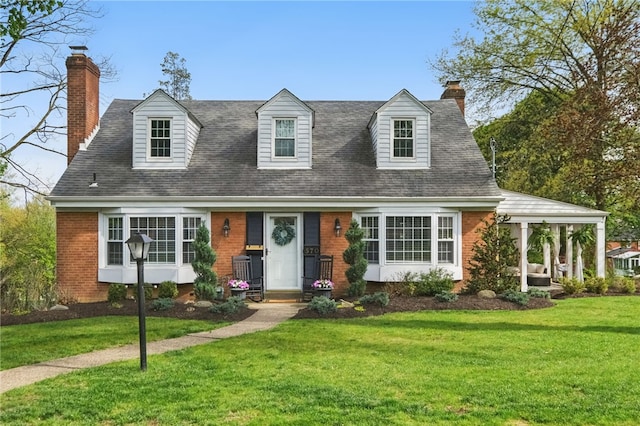 cape cod-style house featuring brick siding, a front lawn, roof with shingles, and a chimney