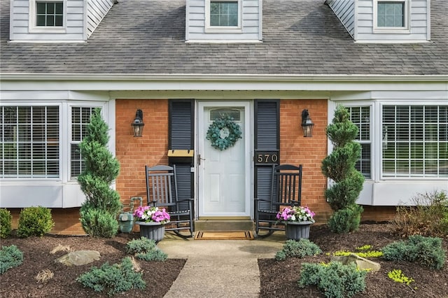 entrance to property featuring brick siding and roof with shingles