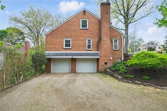 exterior space featuring a garage, a chimney, driveway, and brick siding