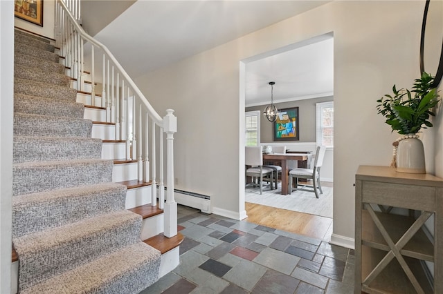stairs featuring a chandelier, stone tile floors, baseboards, a baseboard radiator, and ornamental molding