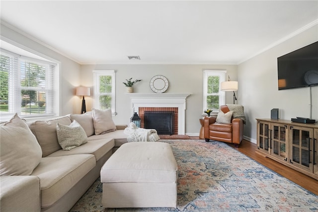 living area with visible vents, a fireplace, wood finished floors, baseboards, and ornamental molding