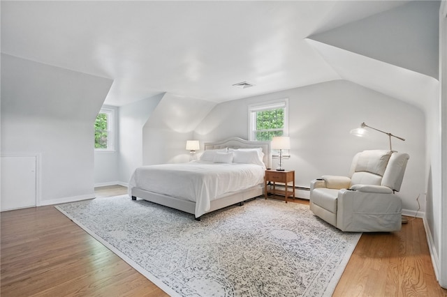 bedroom featuring a baseboard heating unit, lofted ceiling, wood finished floors, and visible vents