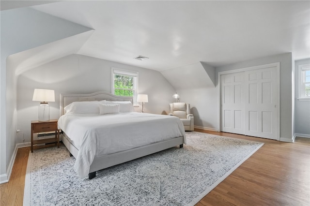 bedroom featuring baseboards, wood finished floors, lofted ceiling, visible vents, and a closet