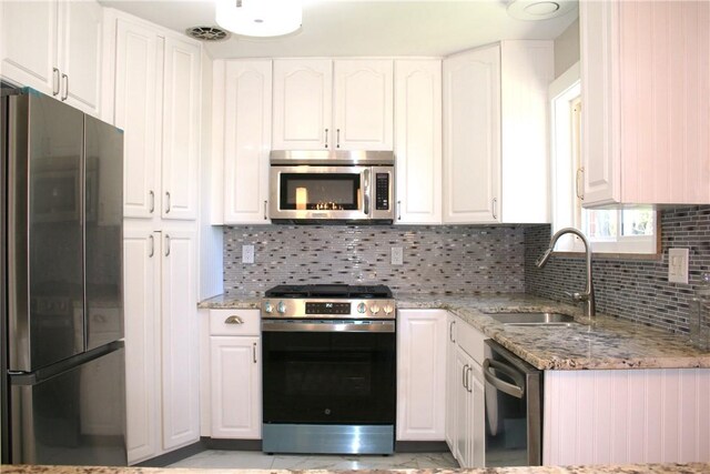 kitchen featuring white cabinets, stainless steel appliances, light stone counters, and a sink