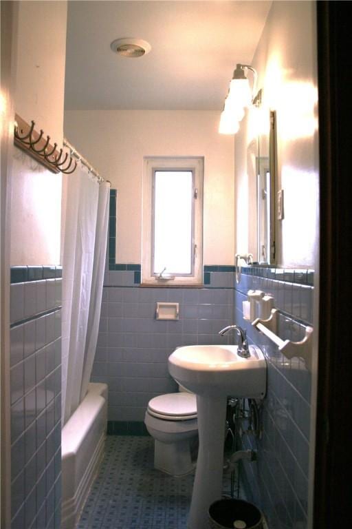 bathroom featuring wainscoting, shower / bath combo, toilet, and tile walls