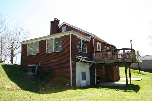 back of house featuring a chimney, a lawn, a wooden deck, brick siding, and cooling unit
