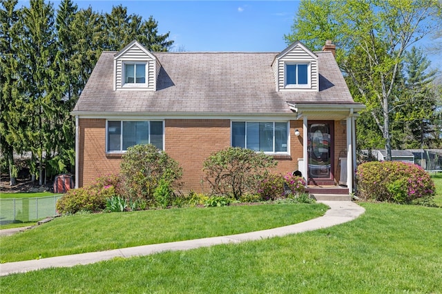 new england style home with brick siding, a front yard, and a chimney
